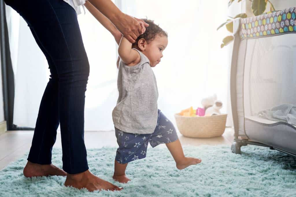 Une maman encourage son bébé à faire ses premiers pas.