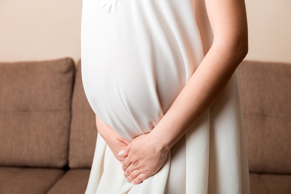 Une femme enceinte en robe blanche est debout sur un canapé.