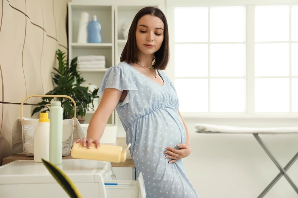 Avant l'accouchement, une femme enceinte se tient devant une machine à laver et réfléchit au mythe ou à la réalité de la nidification.