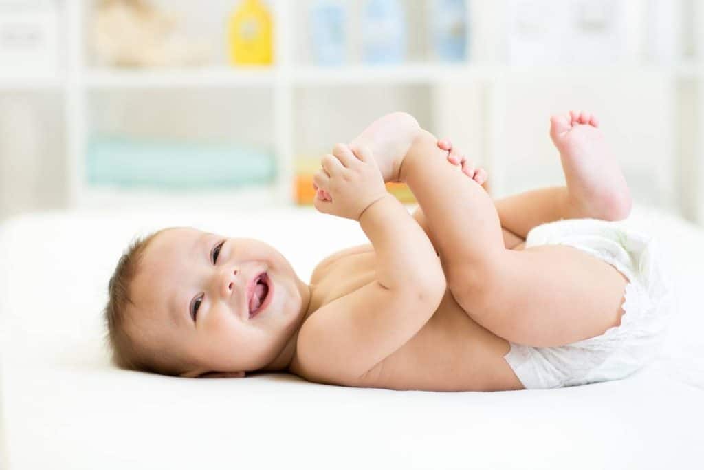 Un bébé à la peau de bébé lisse et douce sourit tout en étant paisiblement allongé sur un lit, évitant tout irritant potentiel.