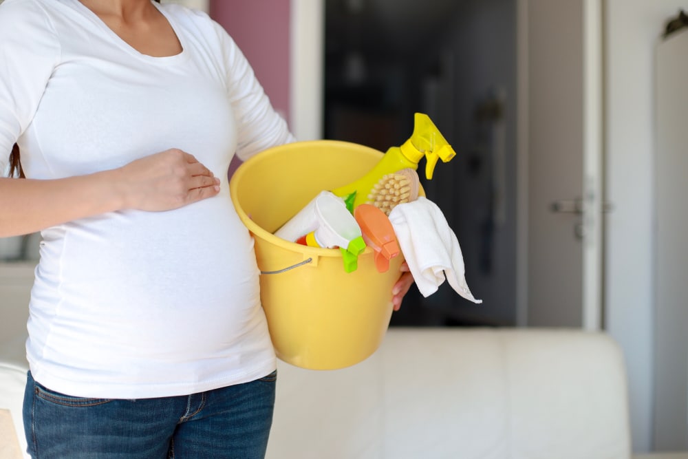 Une femme enceinte tenant un seau de produits de nettoyage. (Mots clés : grossesse, produits d'entretien)