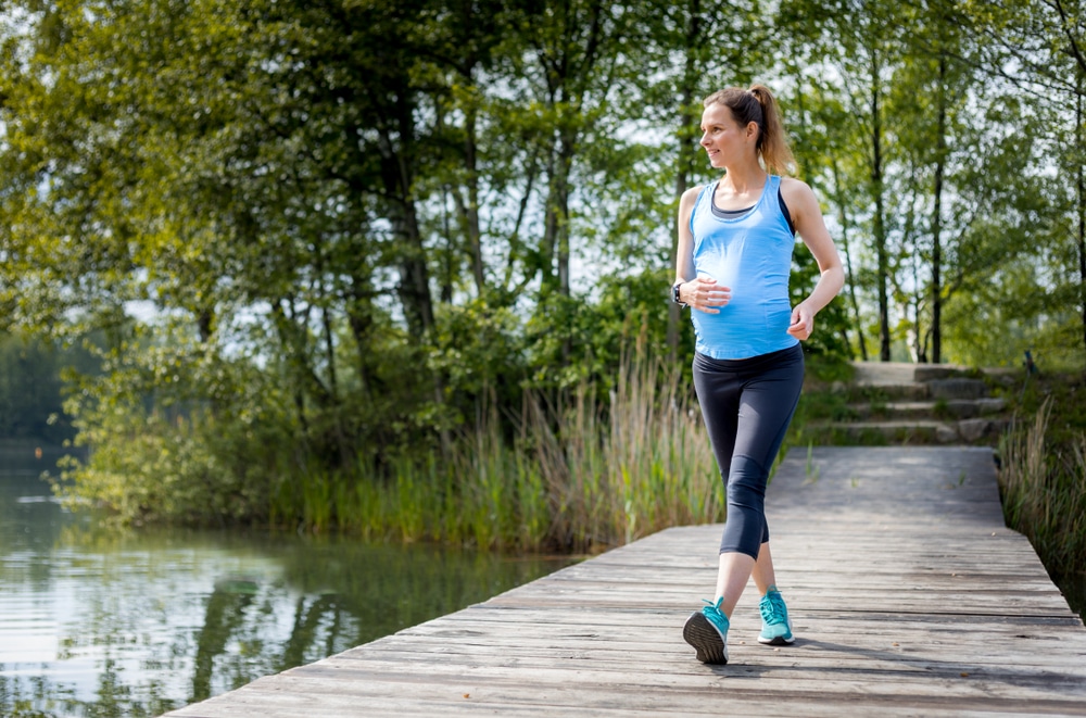 Une femme enceinte fait du jogging sur un quai près d'un lac.