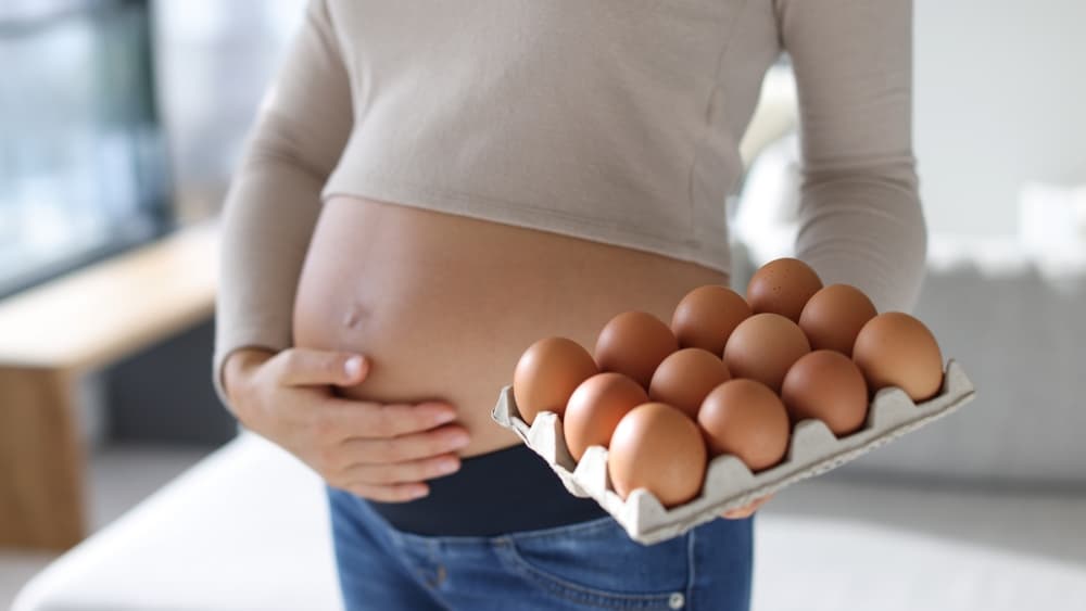 Une femme enceinte tenant une boîte d’œufs.