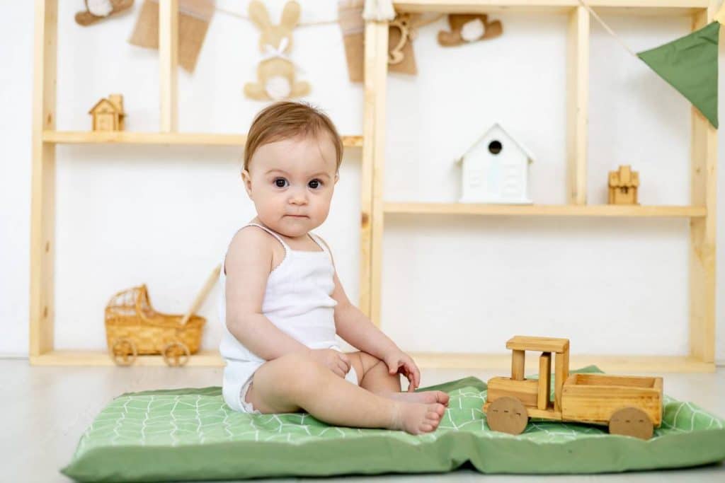 Un bébé est assis sur un tapis vert avec un jouet en bois auto brouillon.