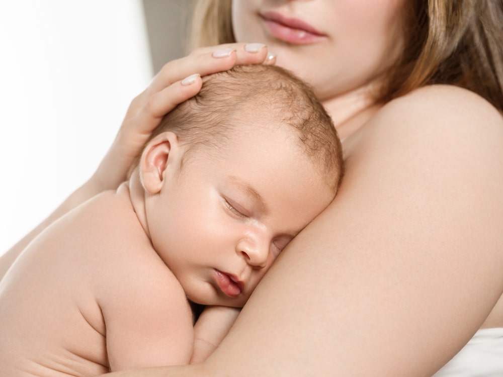 Bébé posé sur l'épaule de sa mère avec un bandeau de peau à peau.