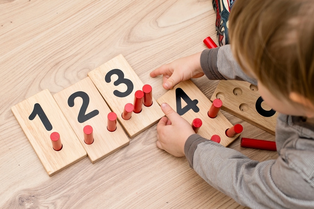 Un enfant place des piquets dans des chiffres en bois pour une activité de comptage dans le cadre de ses jouets éducatifs incontournables.