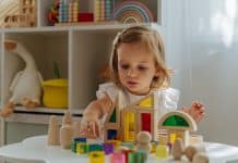 Un enfant concentré sur le jeu avec des blocs de bois colorés, incontournables jouets éducatifs, à une table.