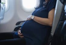 Femme enceinte en chemise bleue prenant un vol près d'une fenêtre d'avion, tenant doucement son ventre.