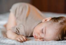 Un tout-petit aux cheveux châtain clair qui dort paisiblement sur un couvre-lit blanc texturé après un repas de rêve.