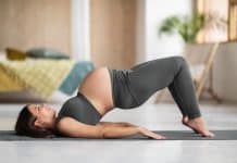 Femme effectuant une pose de pont sur un tapis de yoga lors de sa séance de Pilates prénatale.