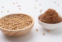 Un bol en bois rempli de graines de soja et un bol blanc contenant de la pâte miso brune, des graines de soja éparpillées sur fond blanc, soulignant l'importance de la sécurité alimentaire enceinte.