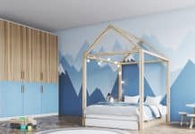 Une chambre d'enfant comprenant un cadre de lit double en forme de maison avec des guirlandes lumineuses, une fresque murale de montagne au mur et des meubles en bois.